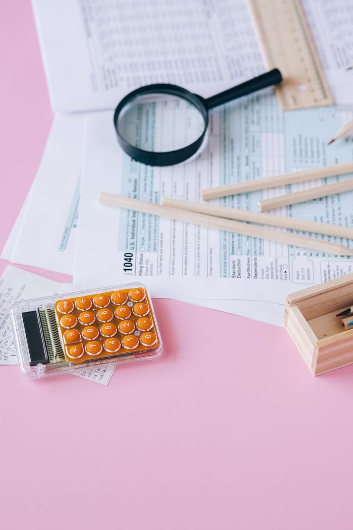 Collection of tax documents with calculator on a pink surface.